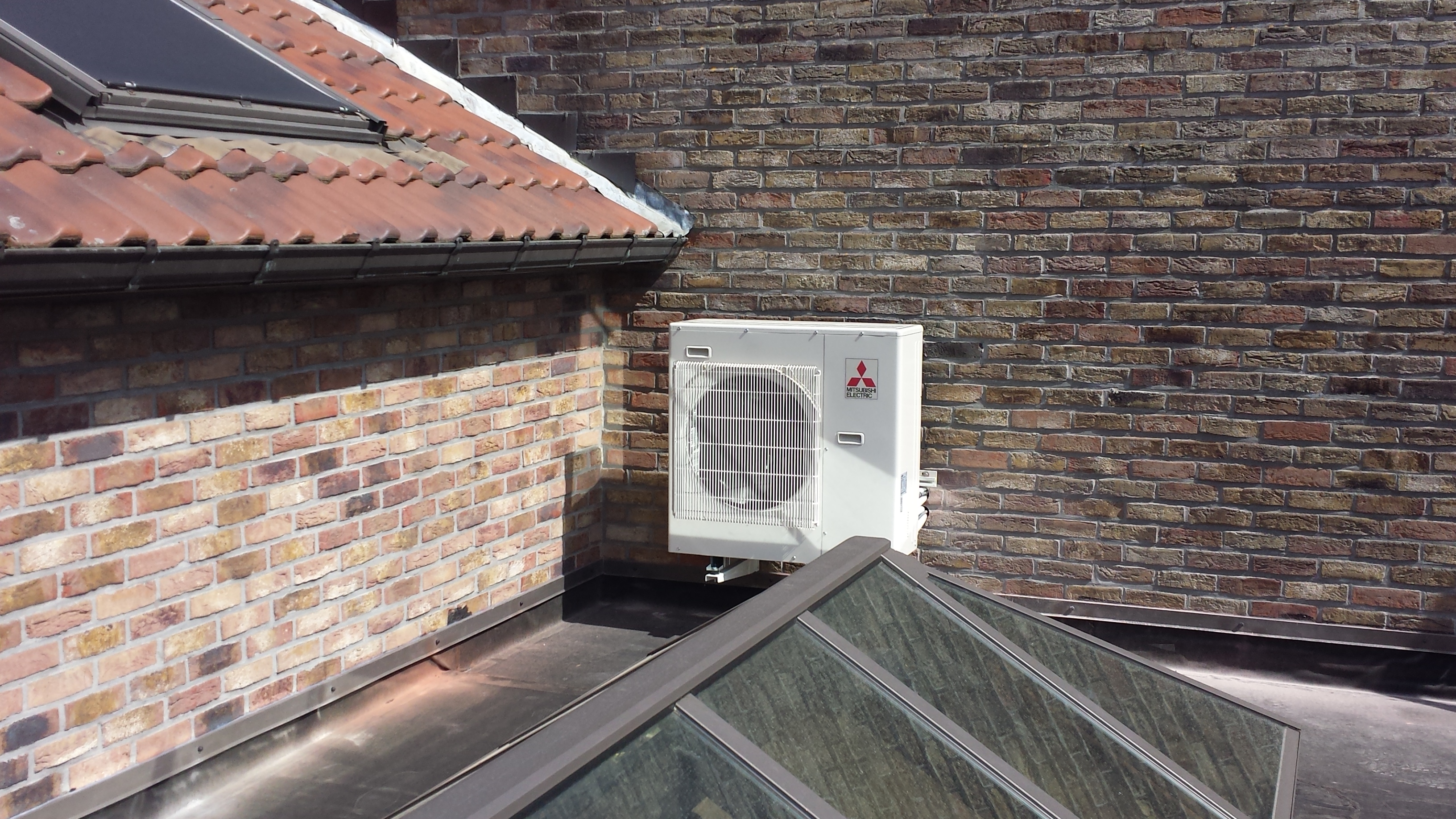 Buitenunit van een warmtepomp op een muurconsole bij de veranda.