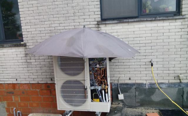 Buitenunit van een warmtepomp tegen een lichte gevel te Ninove.